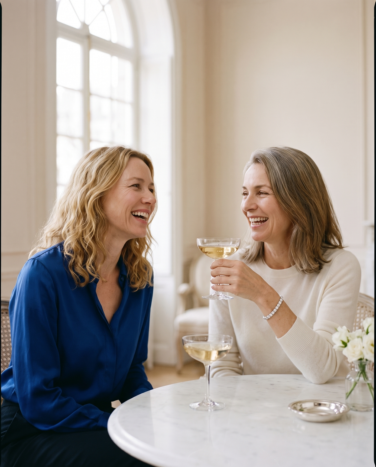 Two women laughing at a marble table, one wearing a moissanite tennis bracelet