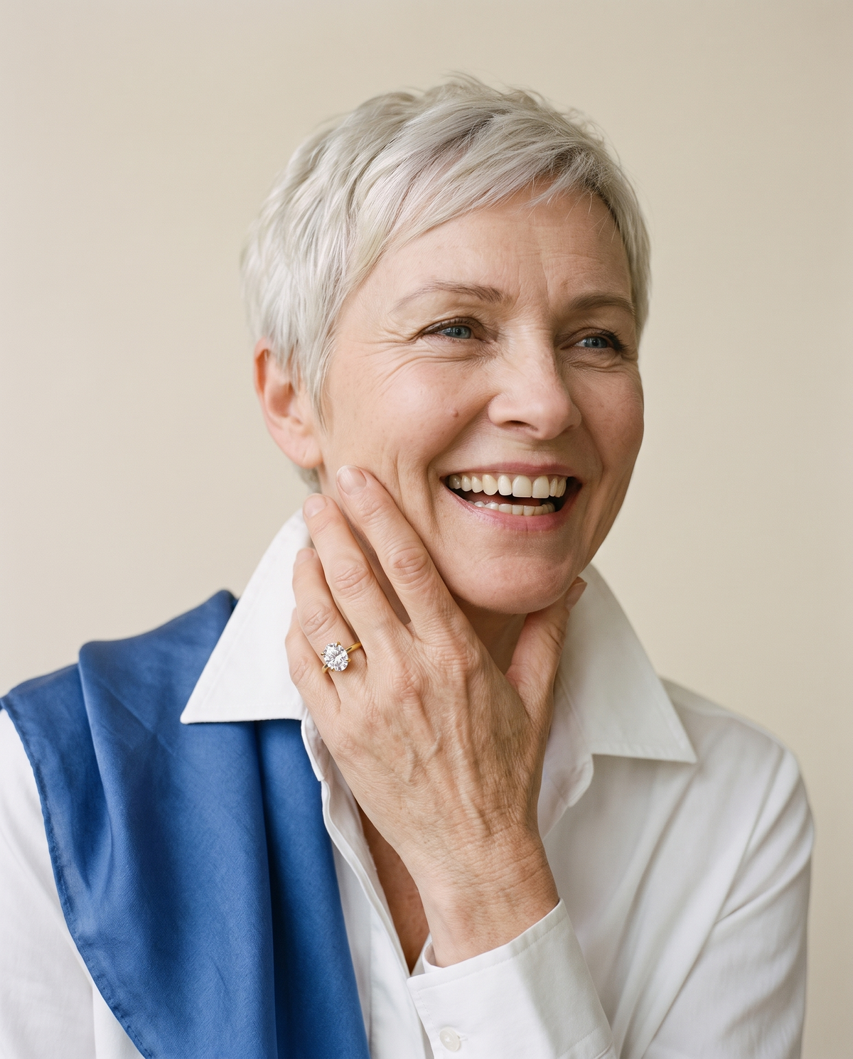 Woman with a silver pixie cut laughing, an oval moissanite ring in yellow gold on her hand